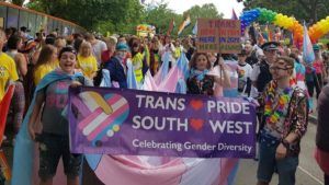 Group of happy brightly-clothed young people on a Pride Parade with a 'Trans Pride' banner