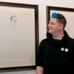 Young man with quiff of bright blue hair looks at a pencil portrait of himself