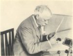 Elderly man with thinning hair and moustache working at his desk
