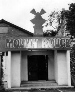 White-painted arched doorway with large "Moulin Rouge" sign and windmill aboveove