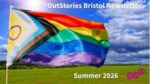 An LGBTQ+ rainbow flag fluttering against a blue sky and a grass field