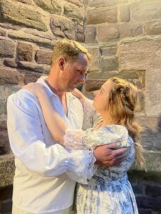 A young man and woman embrace standing in front of a stone wall